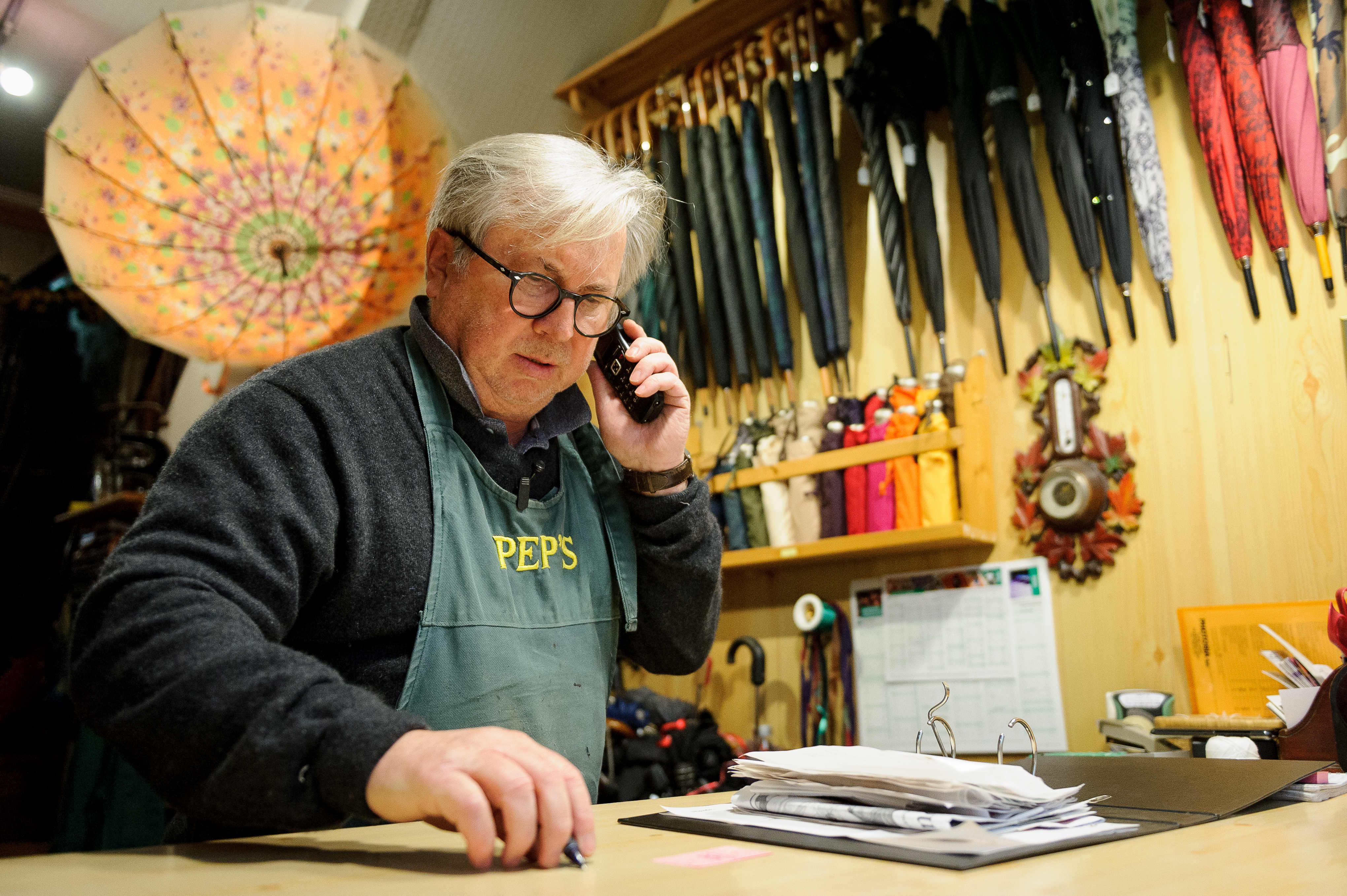 Un artisan en communication avec son téléphone mobile dans son atelier de réparation de parapluie. 