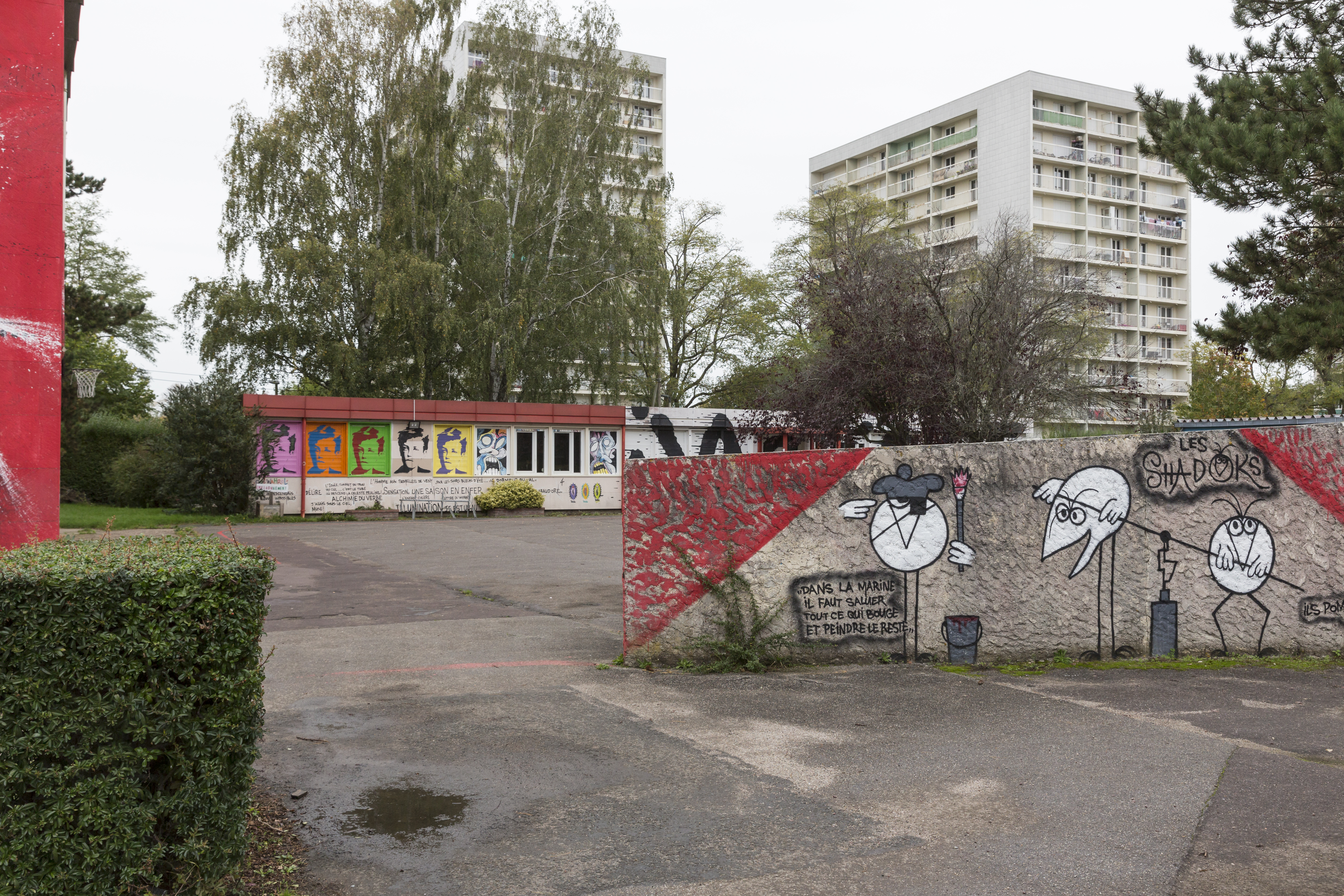 Vu de 2 tous d'habitations dans un quartier populaire, avec au 1er plan des fresques murales qui entourent une cour.