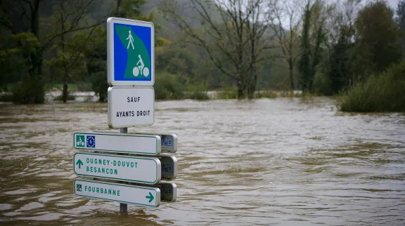 Crue dans un village du Doubs. L'eau est montée jusqu'en haut de panneaux de circulation, avec des arbres en arrière plan.