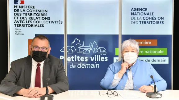 Le ministres J. Gourault et J. Giraud sur un plateau TV avec en fond l'affiche de l'événement; Recontres nationales Petites Villes de demain