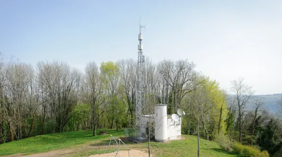 Antenne-relais de téléphonie mobile, entourée d'arbres, de verdure et sous un ciel bleu, sur la colline de la Motte de Vesoul