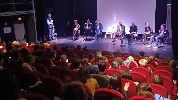 VUe plngeante sur un amphi avec des fauteuils rouges et des personnes sur la scène, lors d'une table ronde