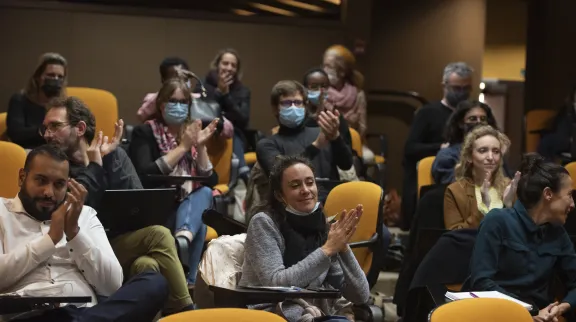 Une foule de gens participant à la rencontre applaudissent. Imls sont sur des fauteuils jaunes