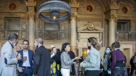 Un grope de personnes discutent dans un grand hall très ouvragé et ancien.