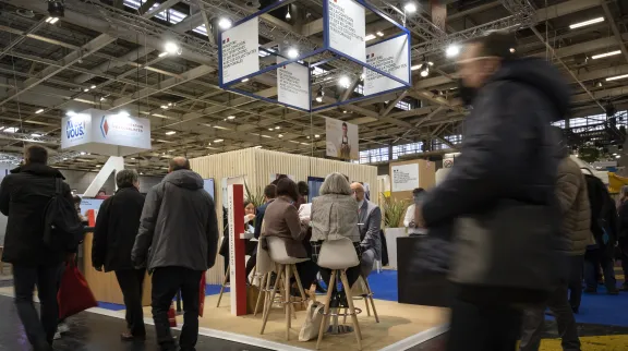 Vue du stand du moinistère depuis une allée du salon des maires et avec des gens, dans un mouvement flouté, qui passent devant.