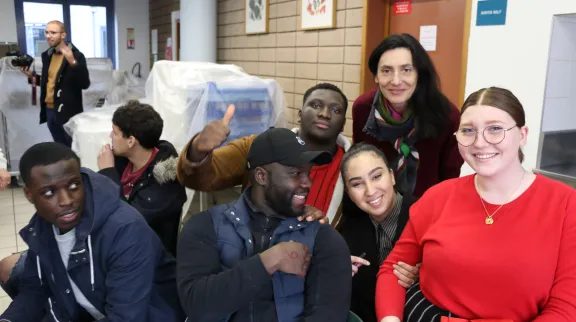 Groupe de lycéens et lycéennes qui posent, assis, avec un adulte accompagnateurs devant une salle de leur lycée.. Ils sont tous souriants. 