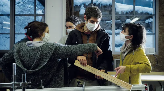 Vue de 3 personnes jeunes dans un atelier, avec une planche en bois