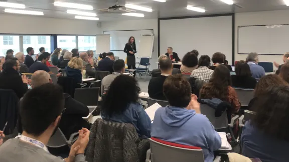 Vue de dos des participants qui sont assis face aux intervenants, qu'on distingue en arrière-plan.